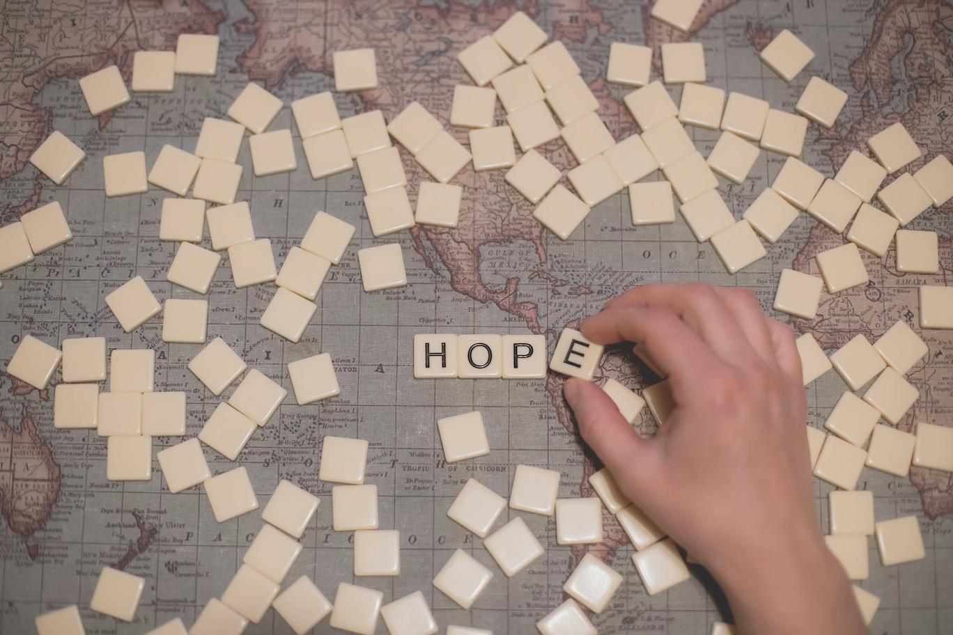 A world map laid out on a table with square tiles on tope of it and four tiles spell hope.