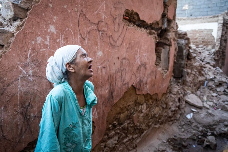 A person reacts, standing beside a damaged wall and piles of rubble, after an earthquake.