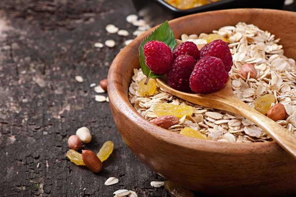 Almond flakes cereals on a wooden bowl with a spoon on top filled with raspberries