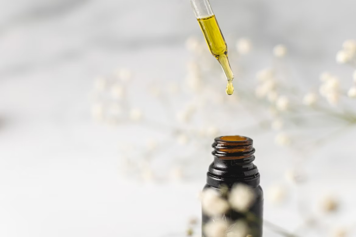 a dropper full of CBD oil dripping back down into the vial with white flowers in the background