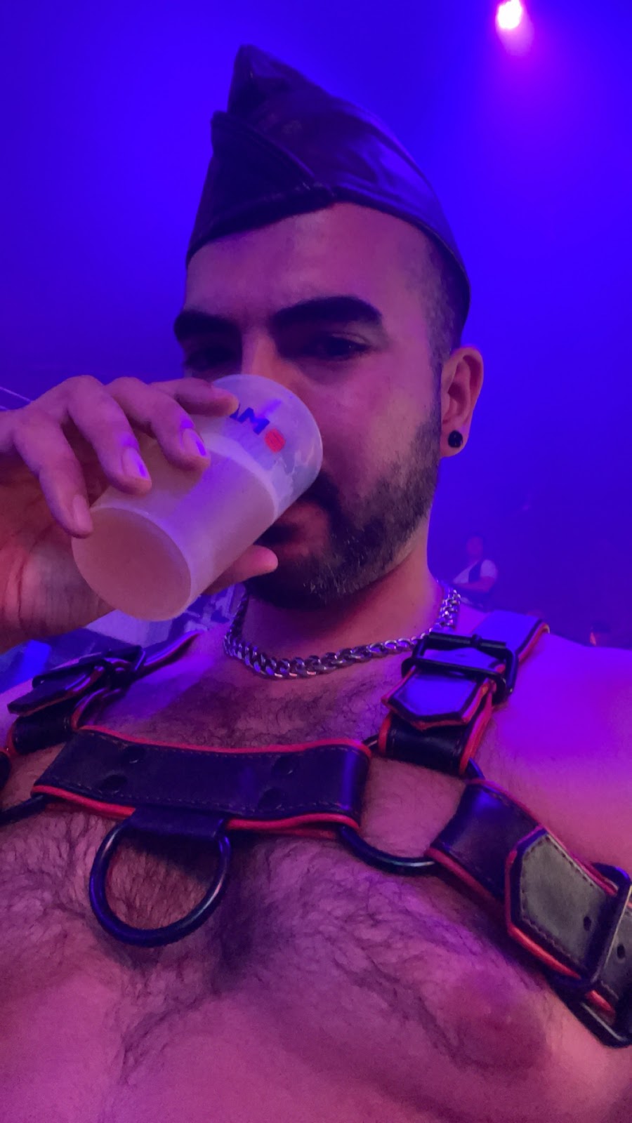 gay onlyfans content creator phil drinking beer and wearing a leather fetish hat and red and black fetish harness at darklands 2024