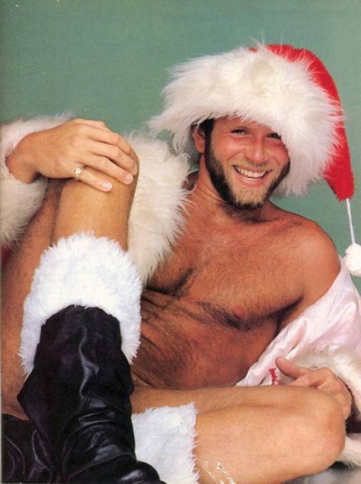 gay naked male laughing and smling for the camera while wearing santa fur trimmed boots and a large santa hat with white fur trim