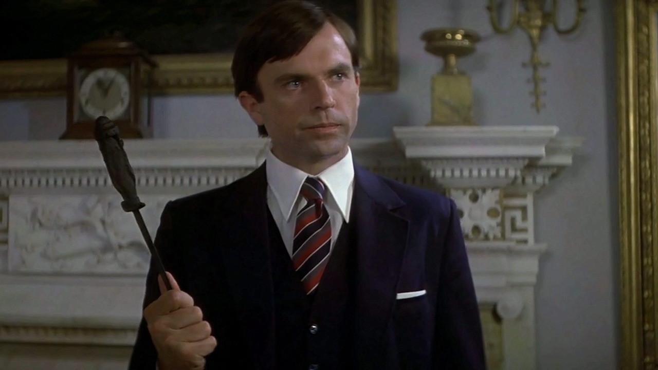 Damien Thorn (Sam Neill), ahora como adulto, vestido con un traje elegante azul y corbata a rayas en La Profecía 3 (1981).
