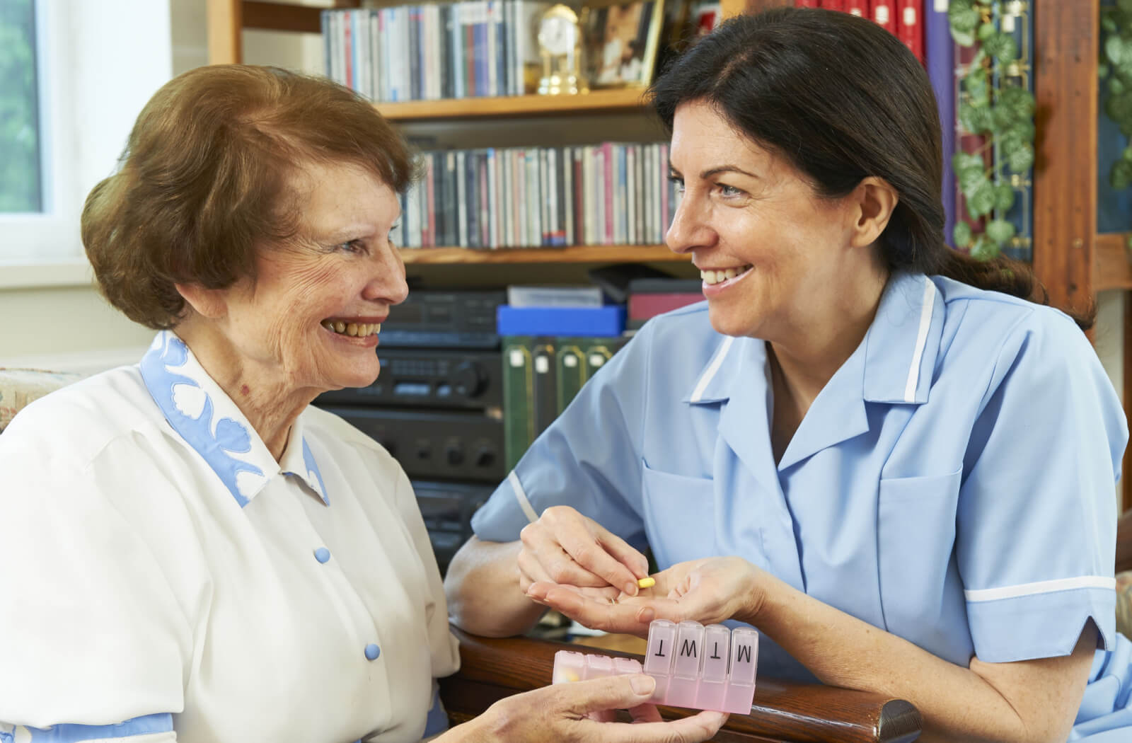An assisted living nurse helping an older adult woman take her medicine.