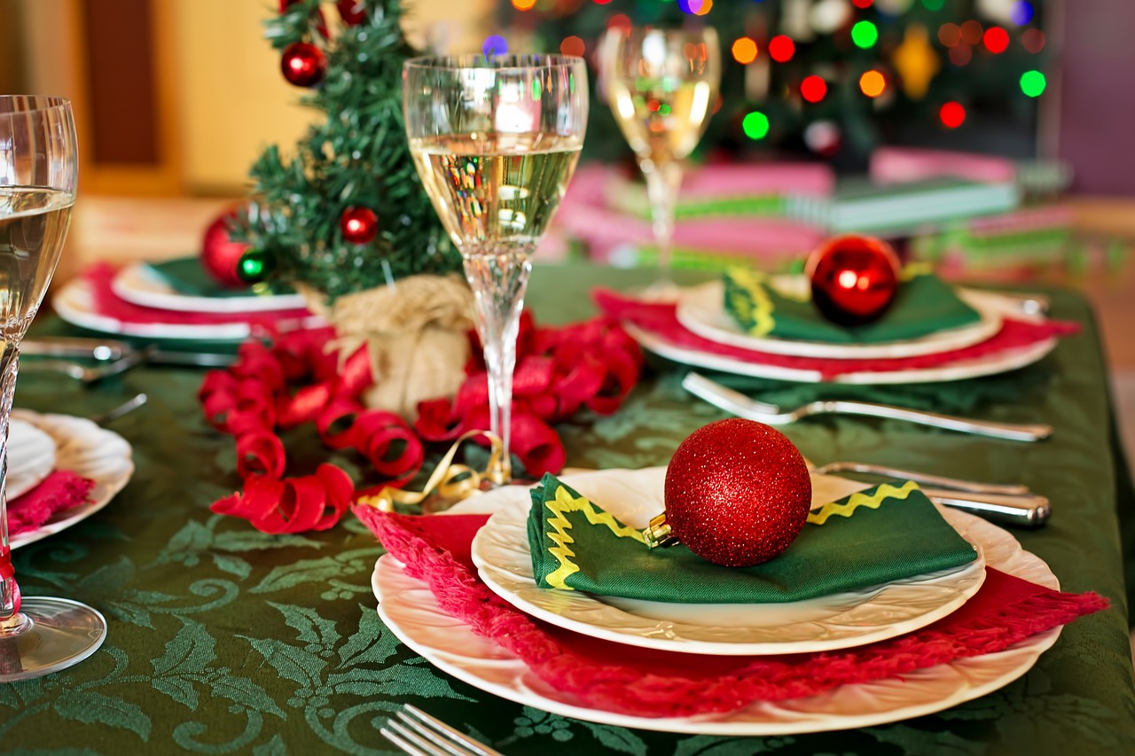 Alt Text: A table with a green tablecloth, white plates with green and red napkins and ornaments, tall clear glasses with white wine in them