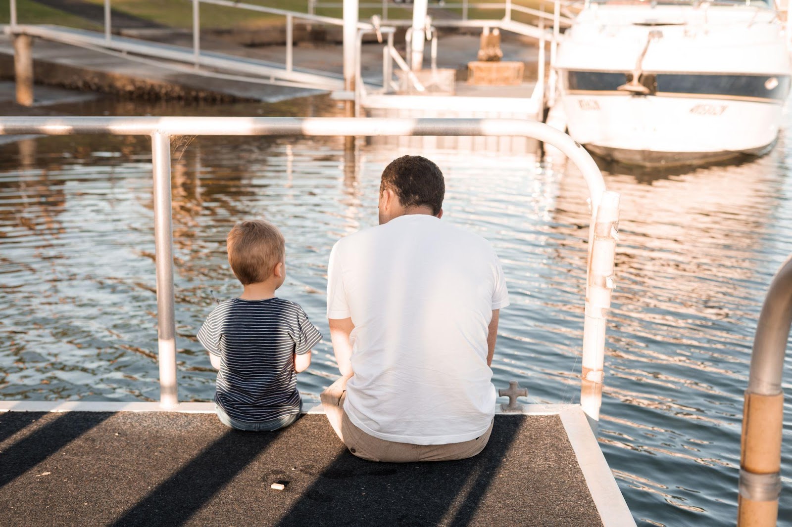Une personne et un enfant assis sur un quai regardant un bateau Description générée automatiquement