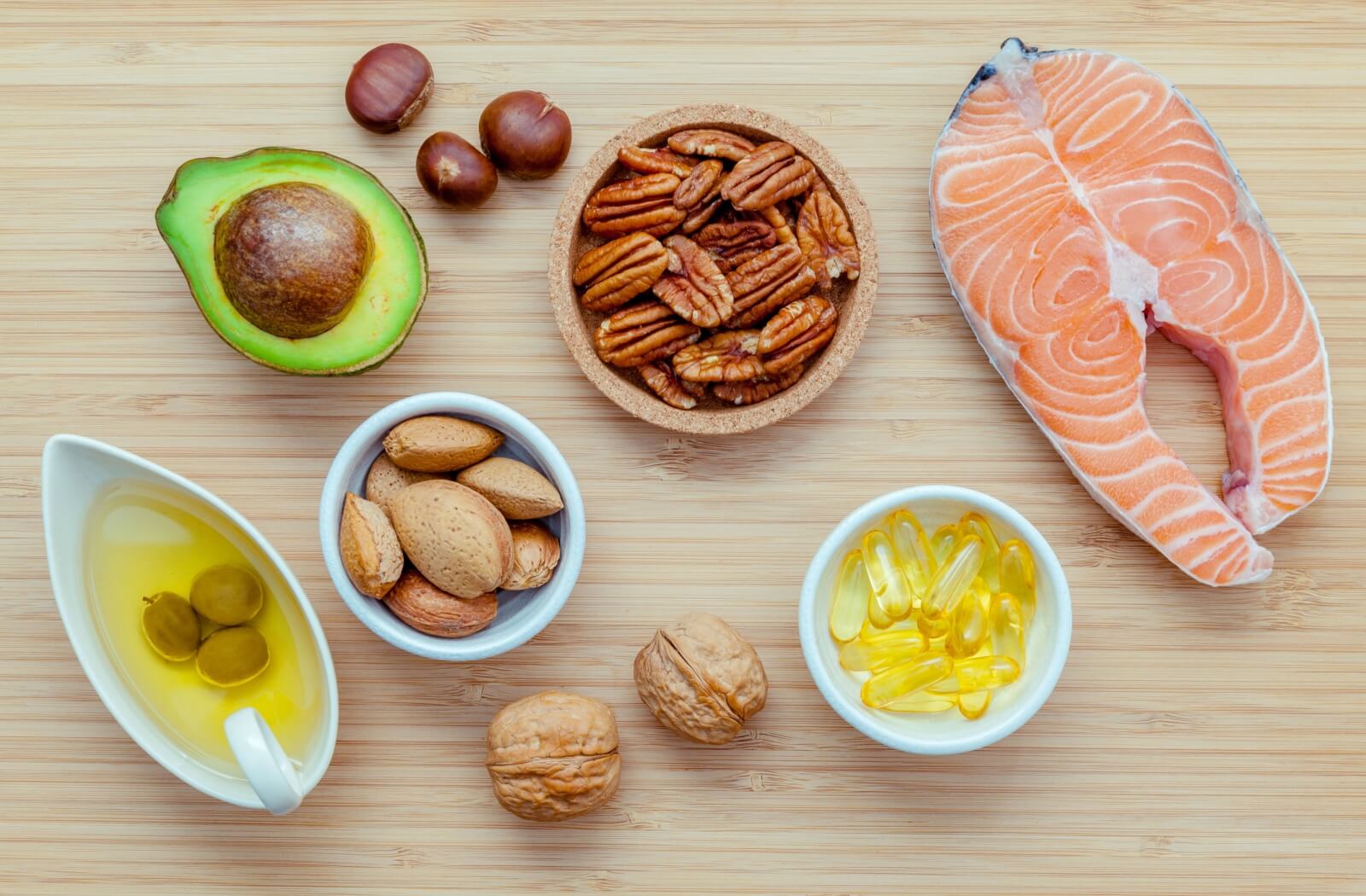 An assortment of food rich in Omega-3 fatty acids and a bowl full of Omega-3 supplements on a wooden backdrop.