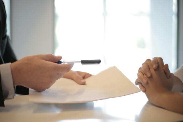 one person handing over pen and paper to other person