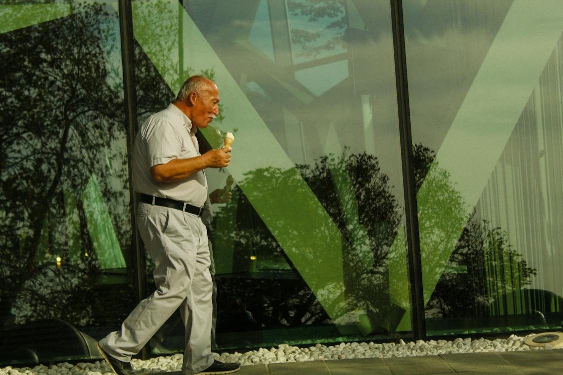 elderly man walking on the sidewalk eating an ice cream