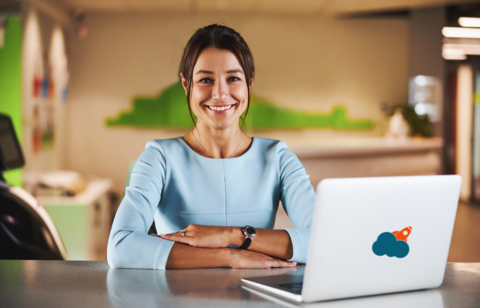 A professional woman smiling at her desk with a laptop, likely providing virtual assistance services.