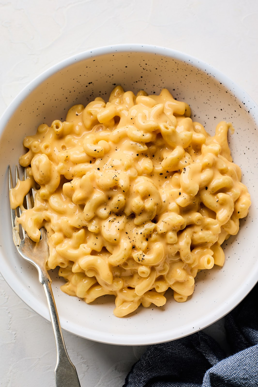A bowl of homemade velvetta mac and cheese recipe with black pepper sprinkled on top and a silver fork
