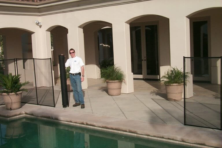 Man in the process of rolling up a mesh removable pool fence section