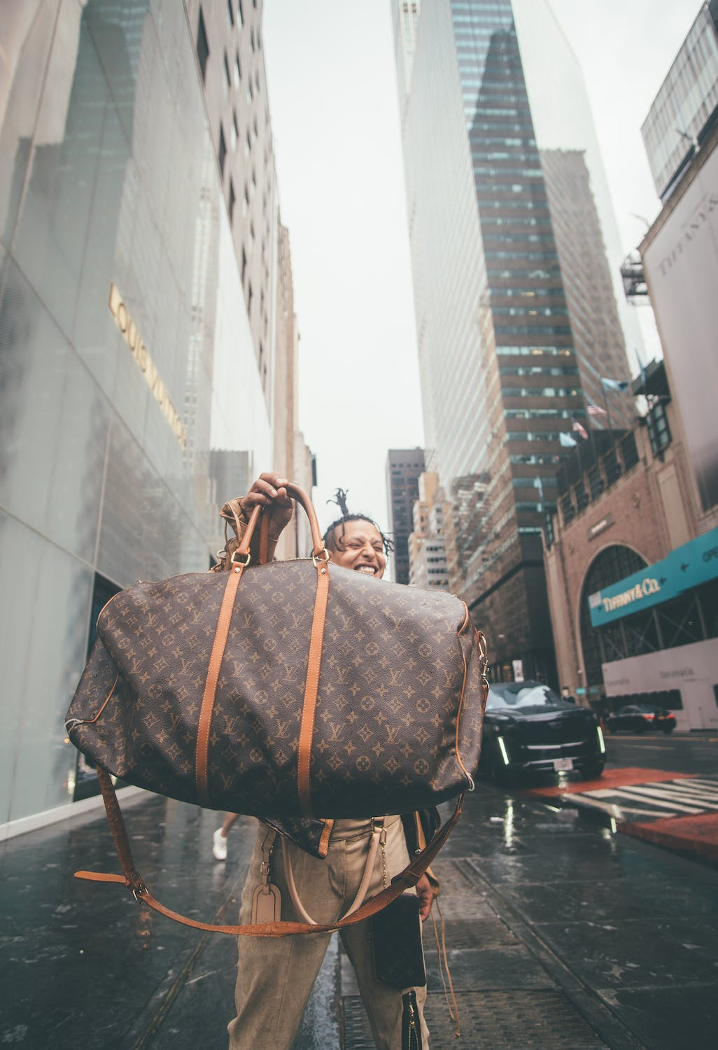 A man laughing and showcasing his Louis Vuitton bag.