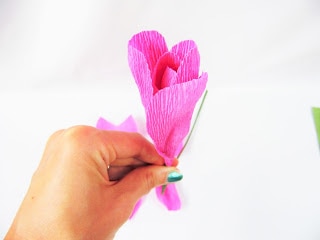Abbi Kirsten holds an unfinished crepe paper rose and wire stem in her hand to show how the petal pieces will form a blooming rose when completed. 