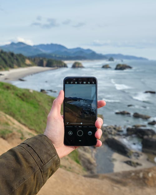 Free Crop person taking photo of seaside scenery on mobile Stock Photo