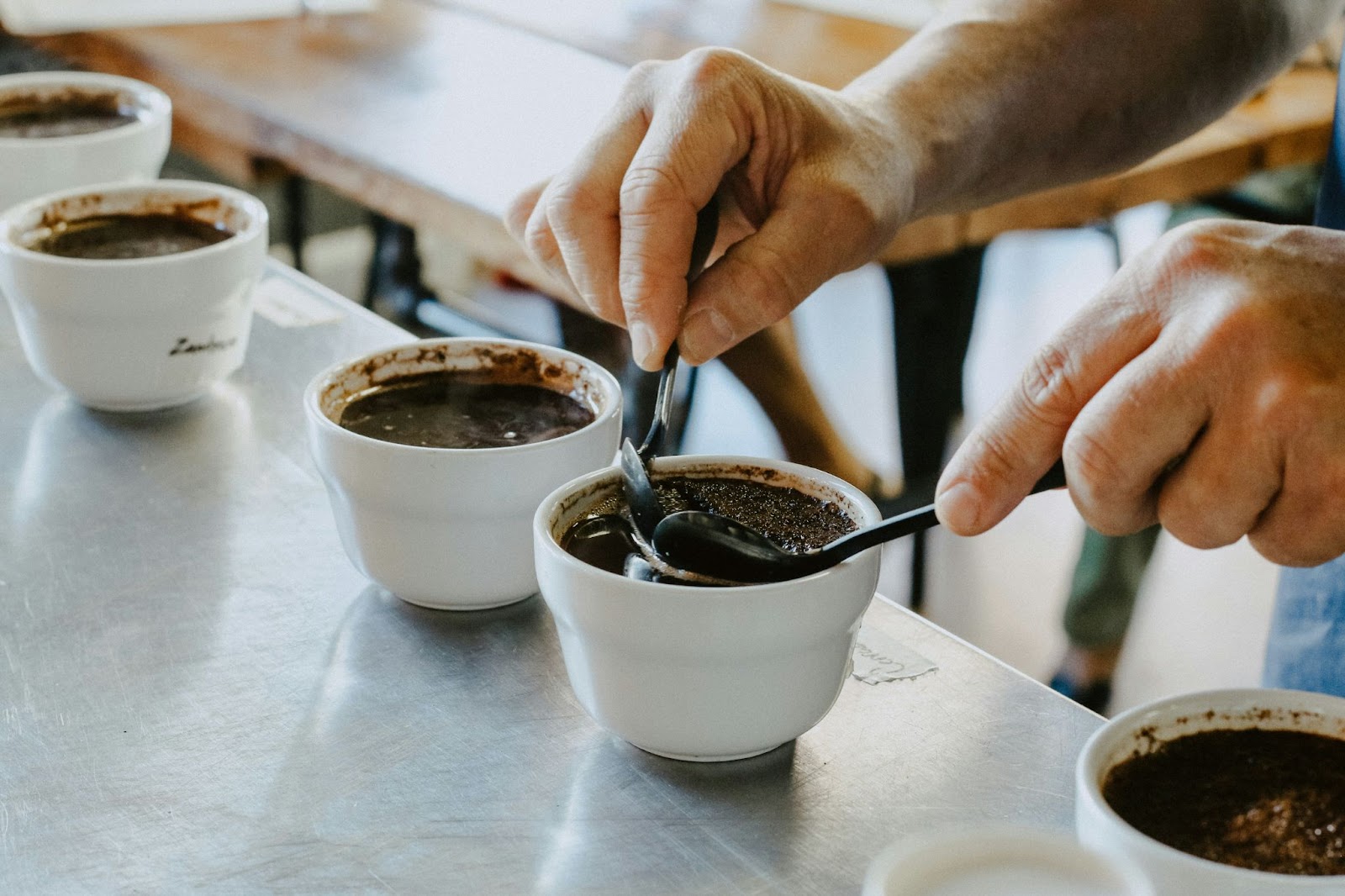 A person cupping coffee, evaluating the brew in white cups with spoons.