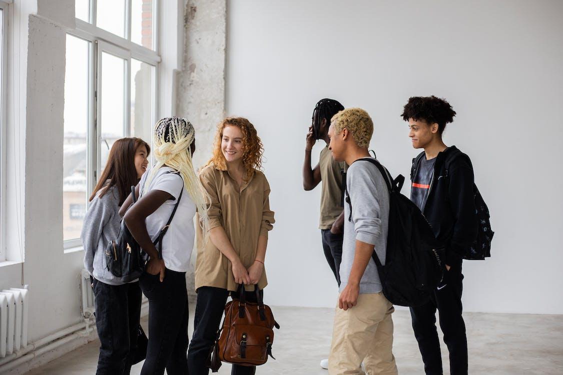Free Group of positive multiracial students with backpacks discussing studying issues after work in team Stock Photo