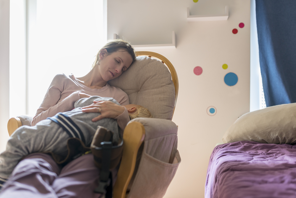 tired mom sleeping with a baby in her arms