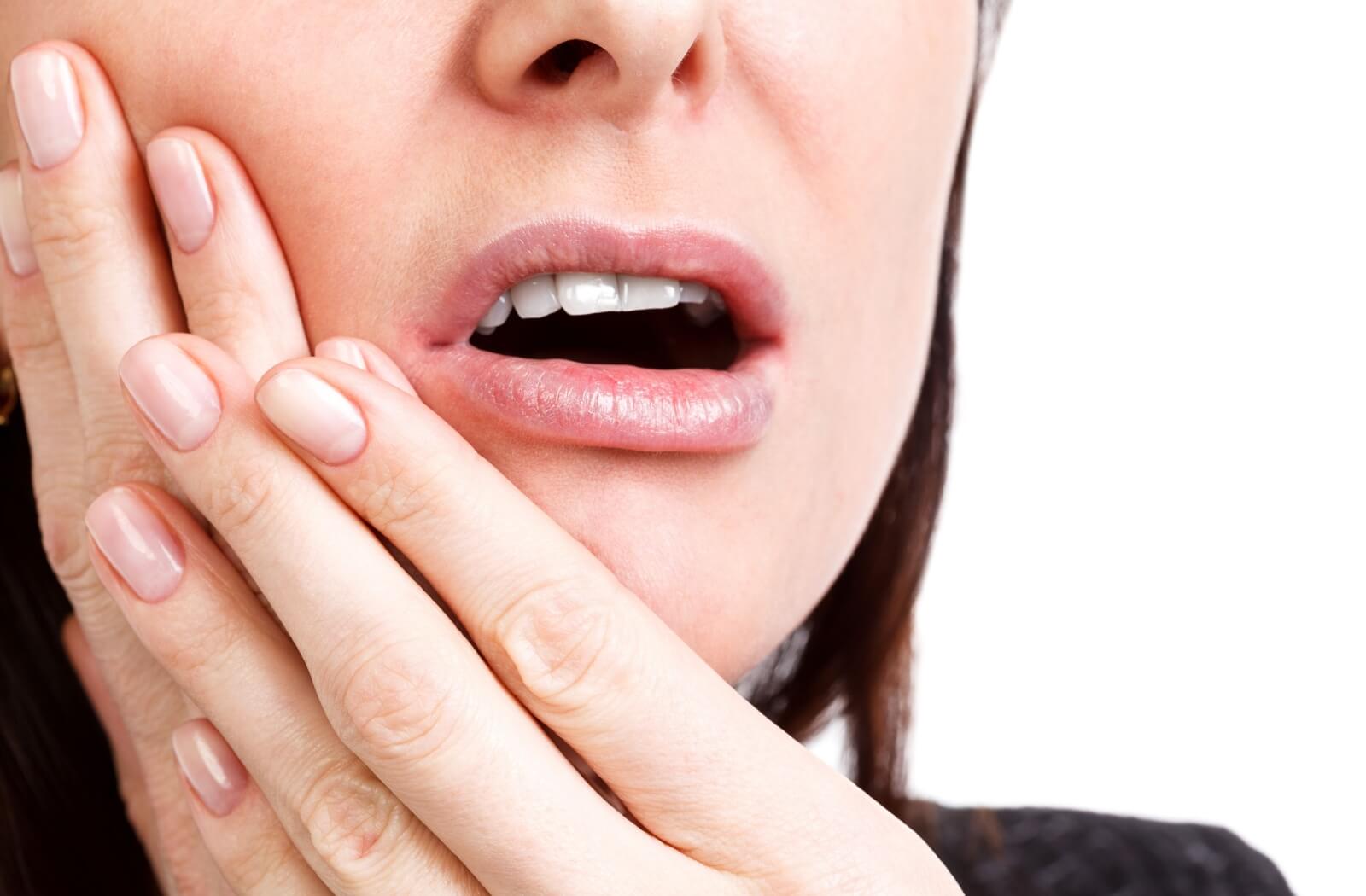 A close-up of a woman applying pressure to her jaw after experiencing toothache.