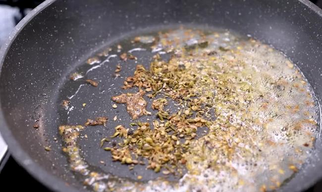 Oil and ghee heating in a pan with cumin seeds and asafoetida starting to crackle