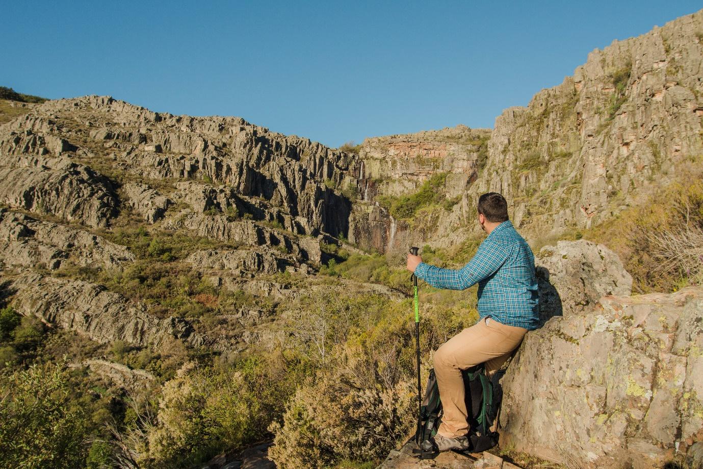 A person sitting on a rock looking at a rocky cliff
Description automatically generated