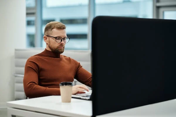 Man with beard working on a large computer monitor in a modern office.