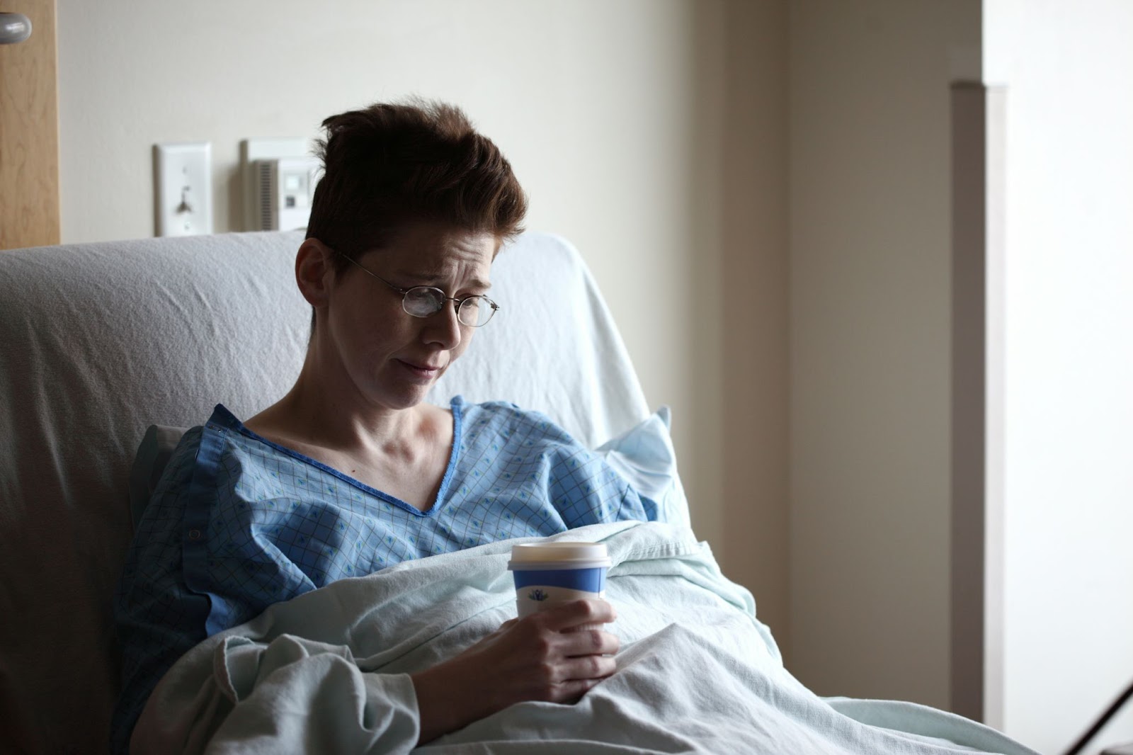 Patient on a hospital bed holding a cup of coffee, crying for her pain and suffering