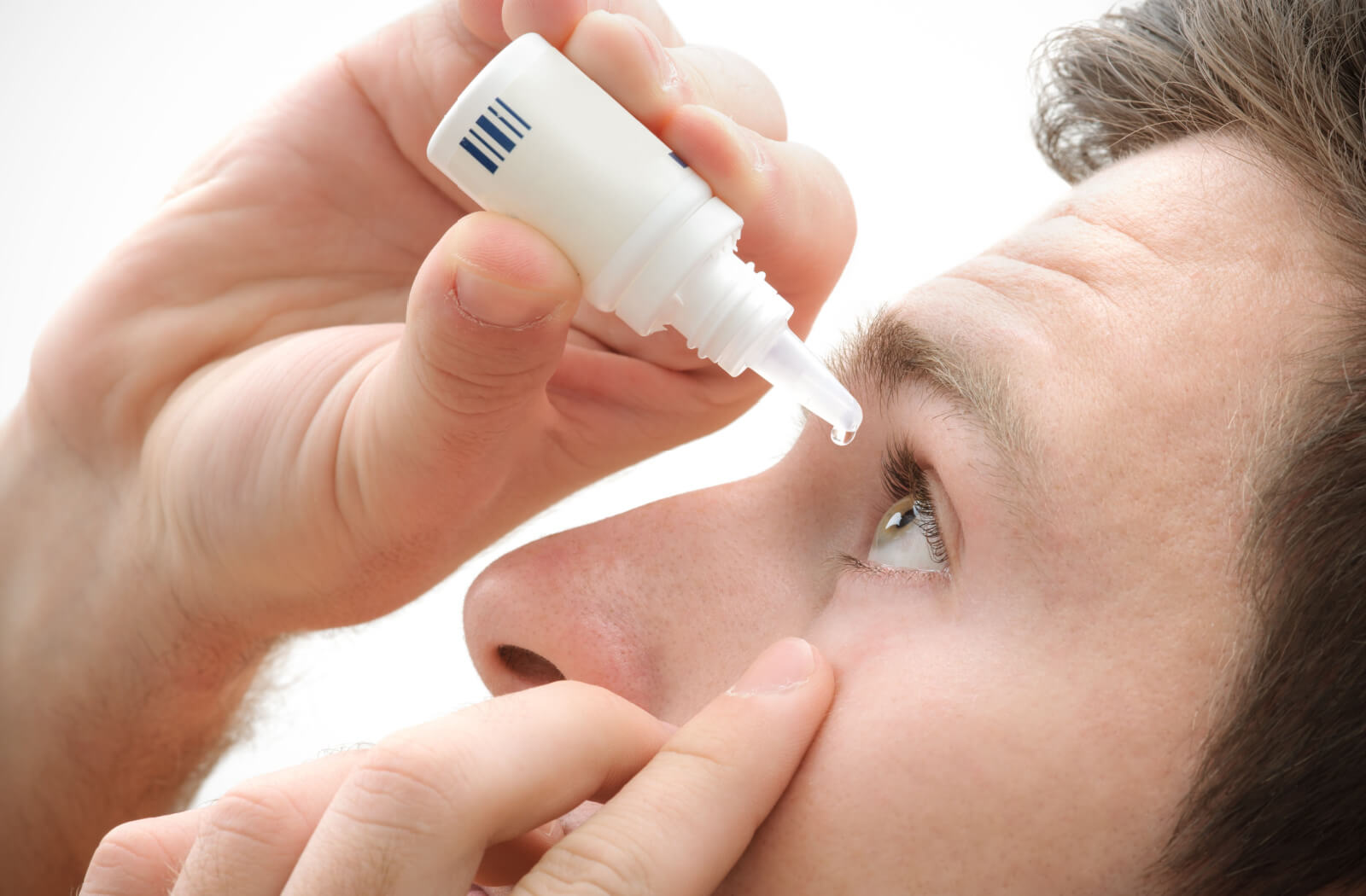 A close-up of a young person applying eyedrops to his left eye.