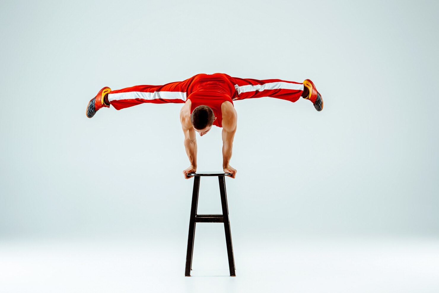 A man doing a handstand split atop a stool.