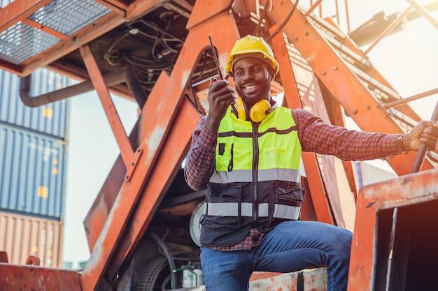 Engenheiro capataz feliz trabalhando operar veículo manipulador de contêineres no pátio de contêineres de carga portuária para envio de importação e exportação