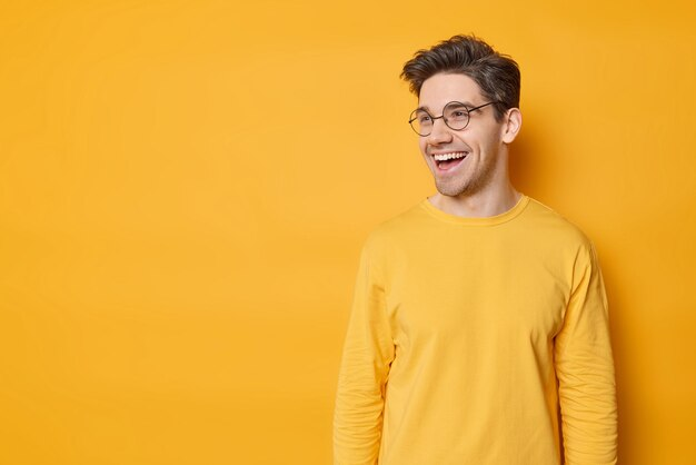 A man with glasses wearing yellow and laughing.