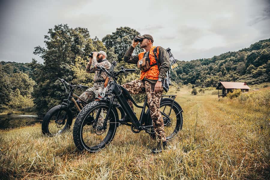 two hunter riding ebikes look through binoculars for quarry