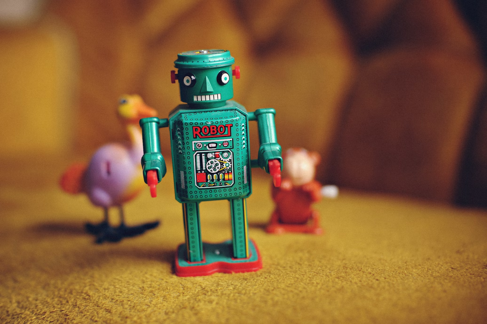 Brinquedo de robô em pé em uma mesa, cercado por outros dois brinquedos desfocados. 