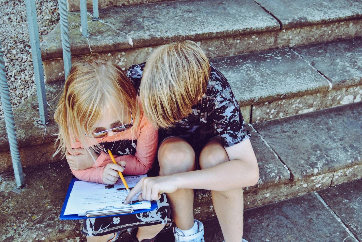 A child and child sitting on steps writing on a book

Description automatically generated