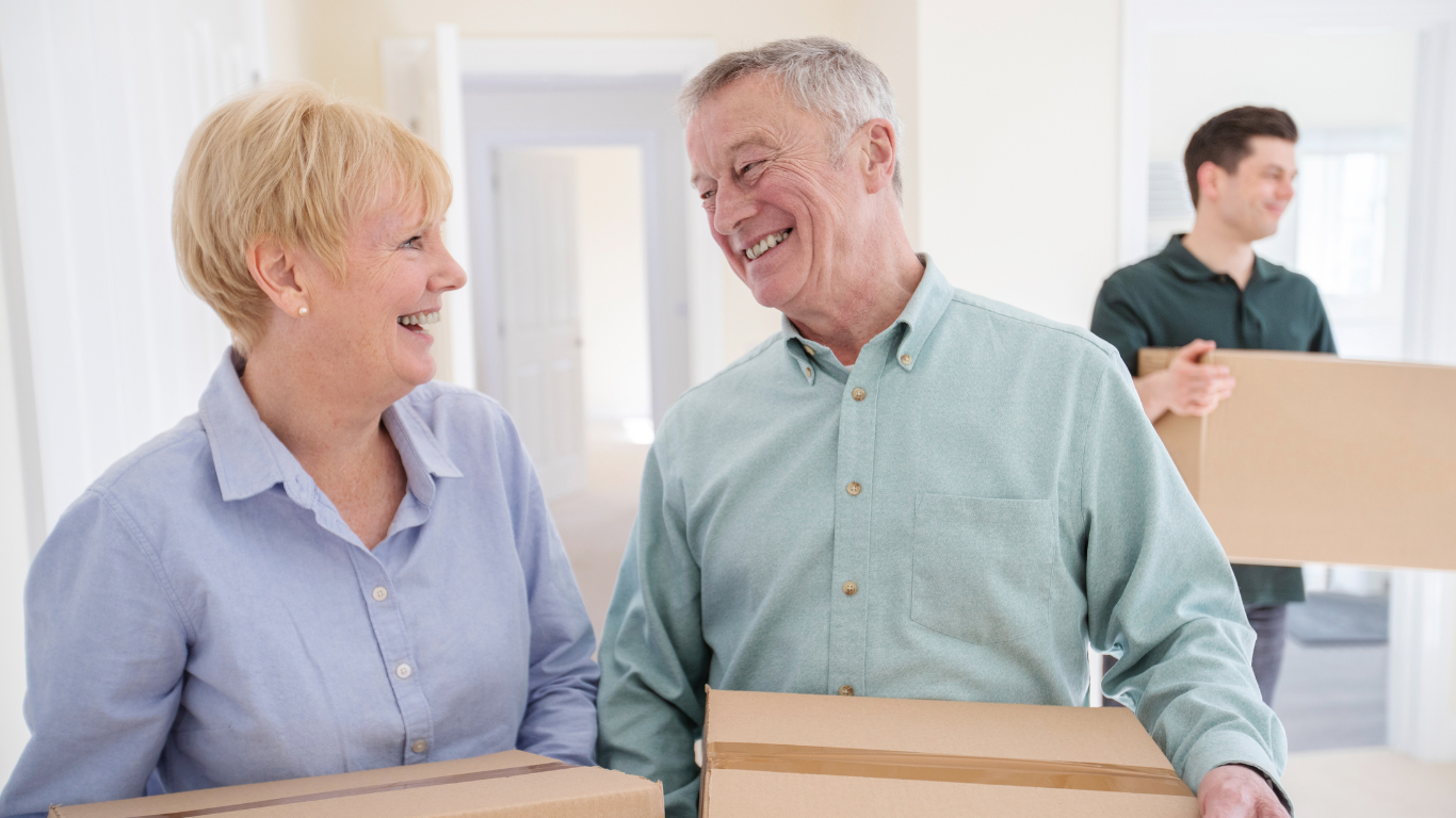 smiling elderly couple carrying moving boxes