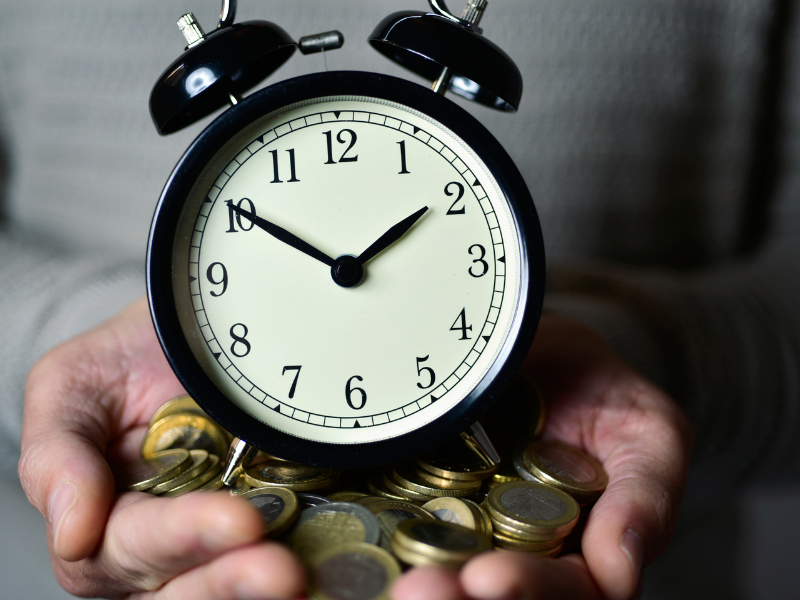 A caucasian man holding an alarm clock with coins in his hands.