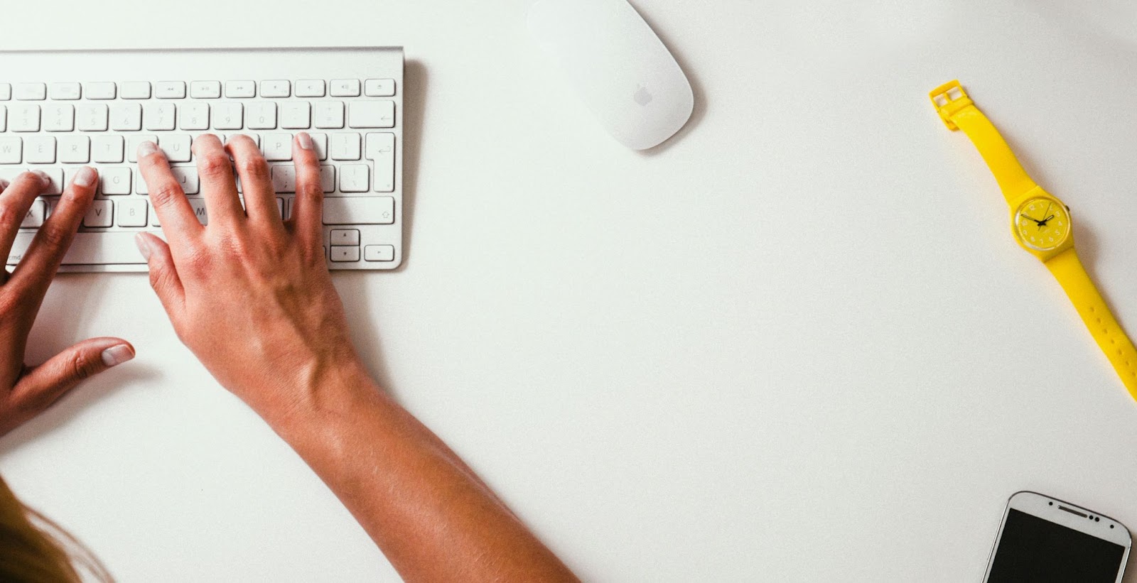 Manos escribiendo en teclado sobre mesa blanca