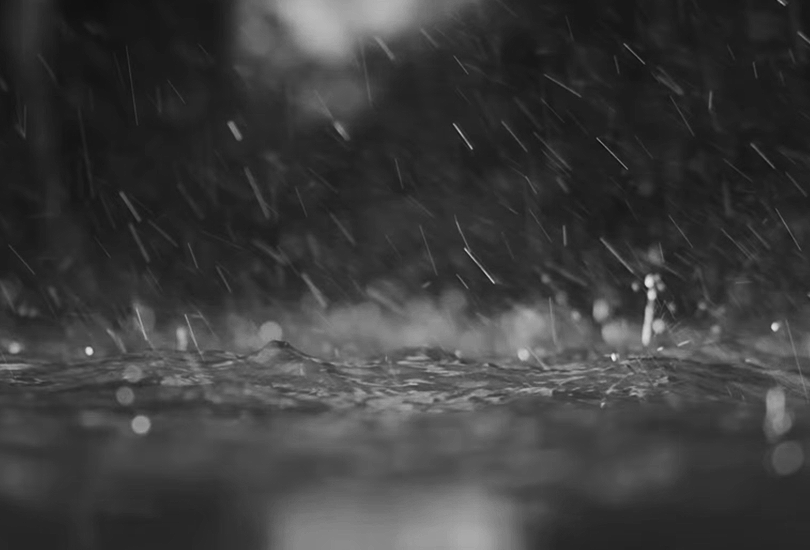 A desaturated screenshot from Kelela's music video for "Enough for Love". Featuring a close-up shot of water in a swimming pool, as it rains down.