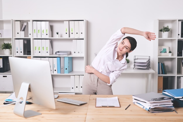  energetic young woman stretching arm  while doing warm-up exercise in office - maintaining work life balance 