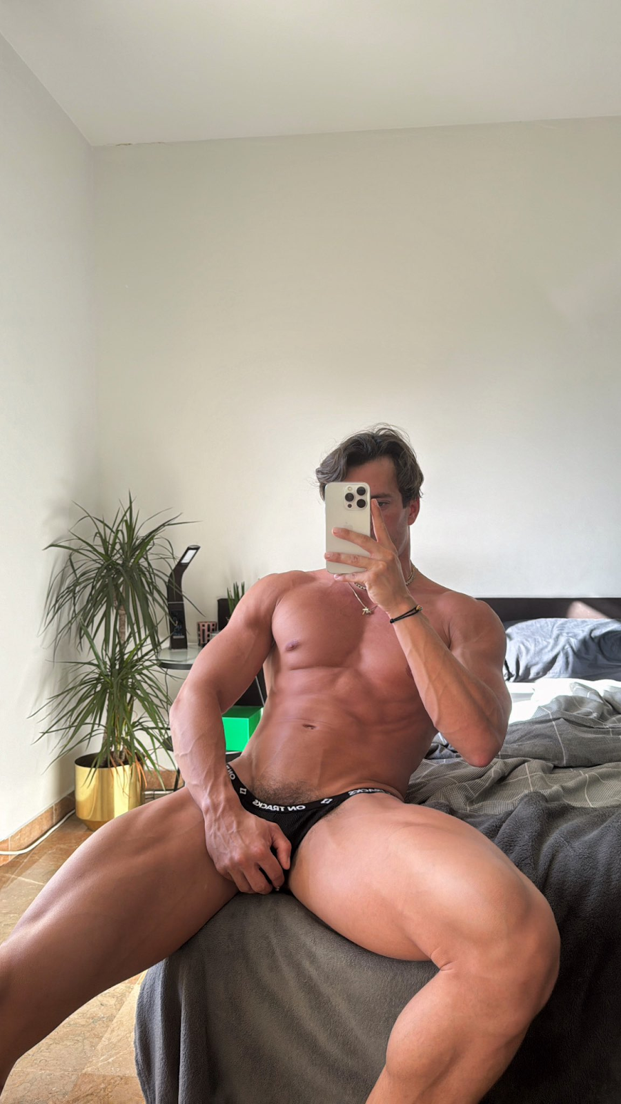 Eric Rmgr sitting on the bed in tiny little black udnerwear grabbibg his crotch taking a photo for social media and gay xxx onlyfans page