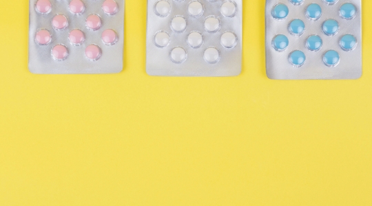 White, pink, and blue pills on a yellow background