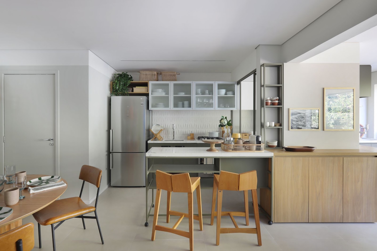 Cozinha americana com paredes, pisos e armários em tons claros. A mesa e cadeiras são de madeira. 