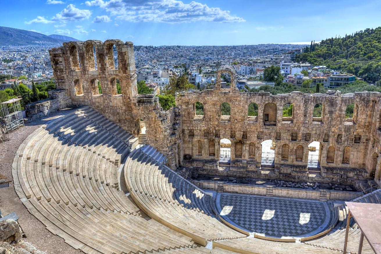 An old stone amphitheater with a city in the background

Description automatically generated