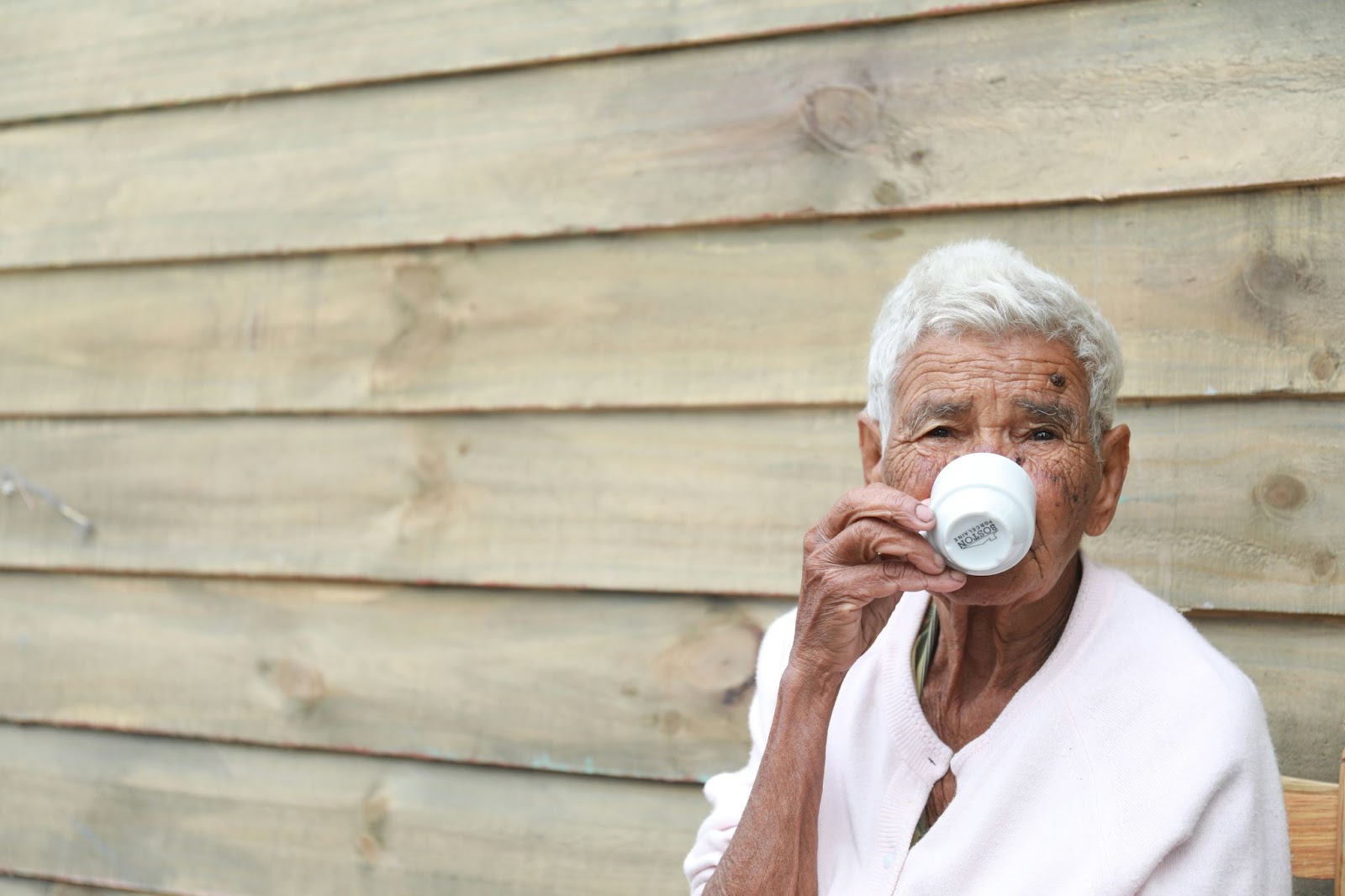 Elderly woman drinking coffee from a cup labeled "Café Santo Domingo.