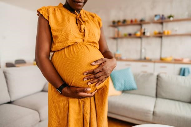 Black Woman Enjoying Pregnancy At Home Portrait of beautiful pregnant black mother holding her pregnant belly at home. Close-up. pregnancy stock pictures, royalty-free photos & images