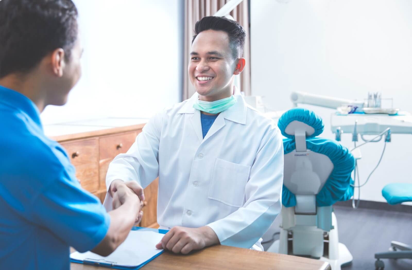 A man in an dentist's office shaking hands with his male dentist