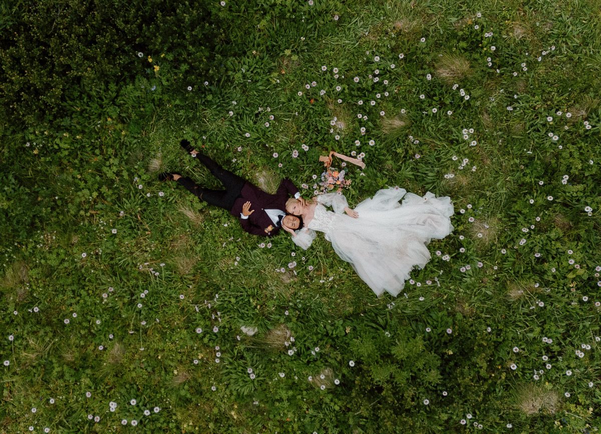 drone shot photography of couple in their wedding attire laying down in the grass 