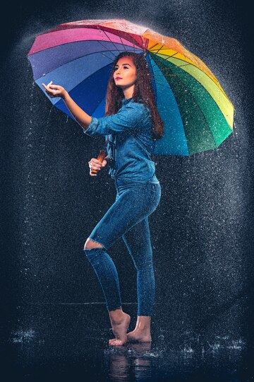 A girl enjoying rain and holding a rainbow umbrella.