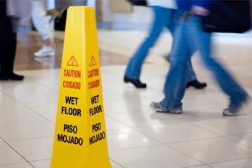 people walking fast past a wet floor sign