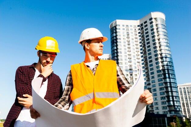 Medium shot low angle view of engineer and architect looking at plans